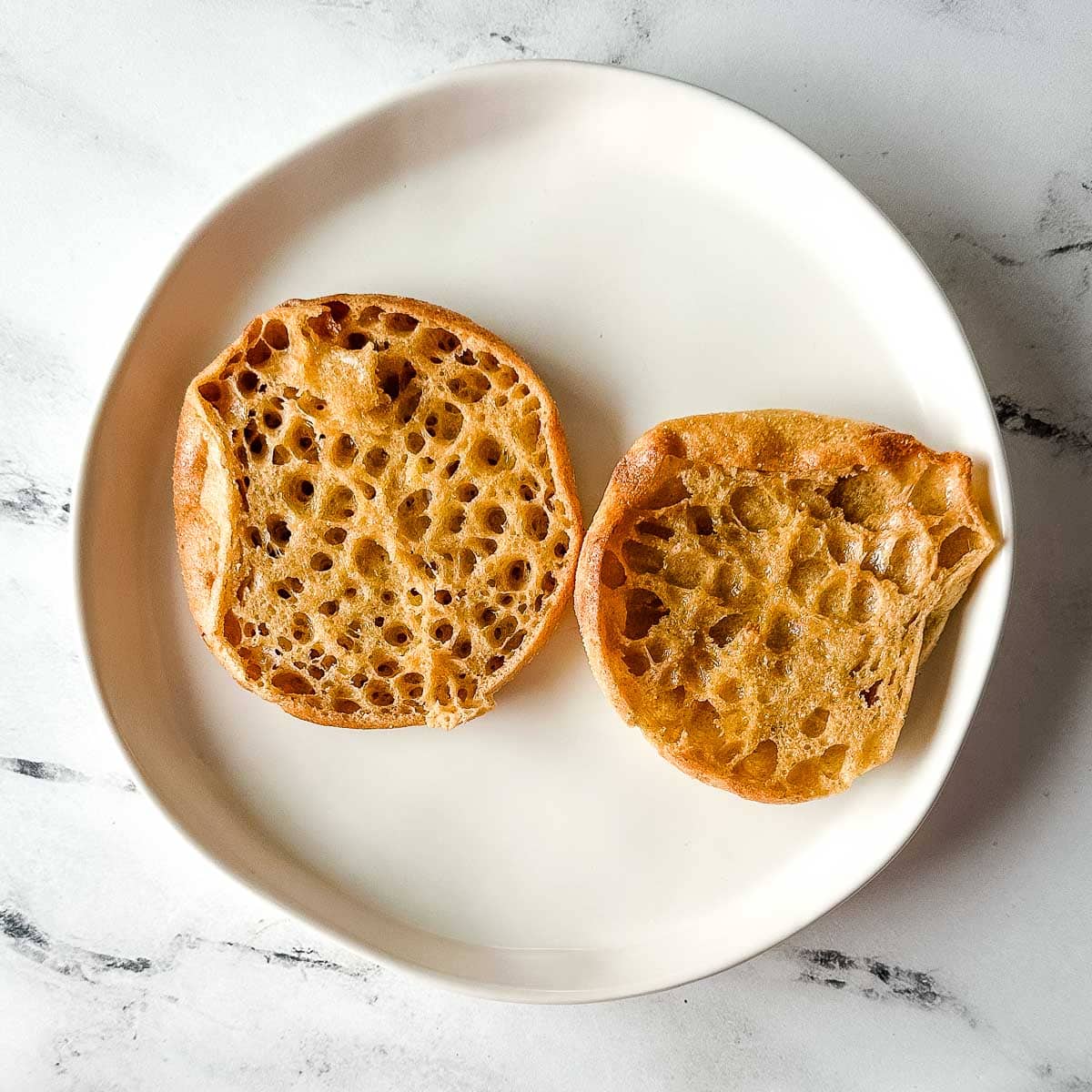 Toasted and buttered English muffin on a white plate.