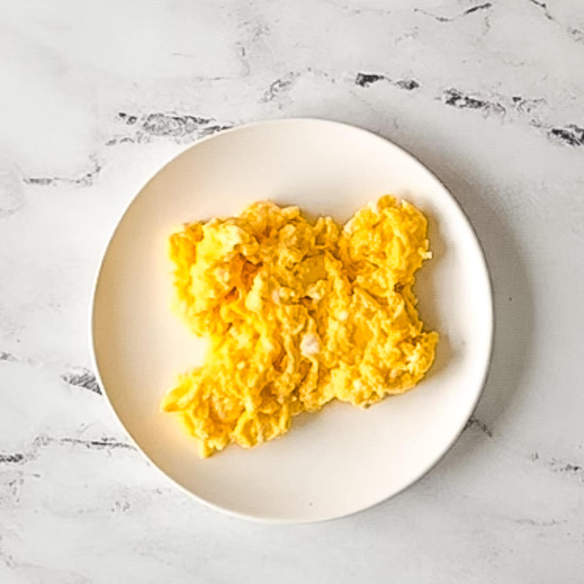 cooked scrambled eggs on a white plate.