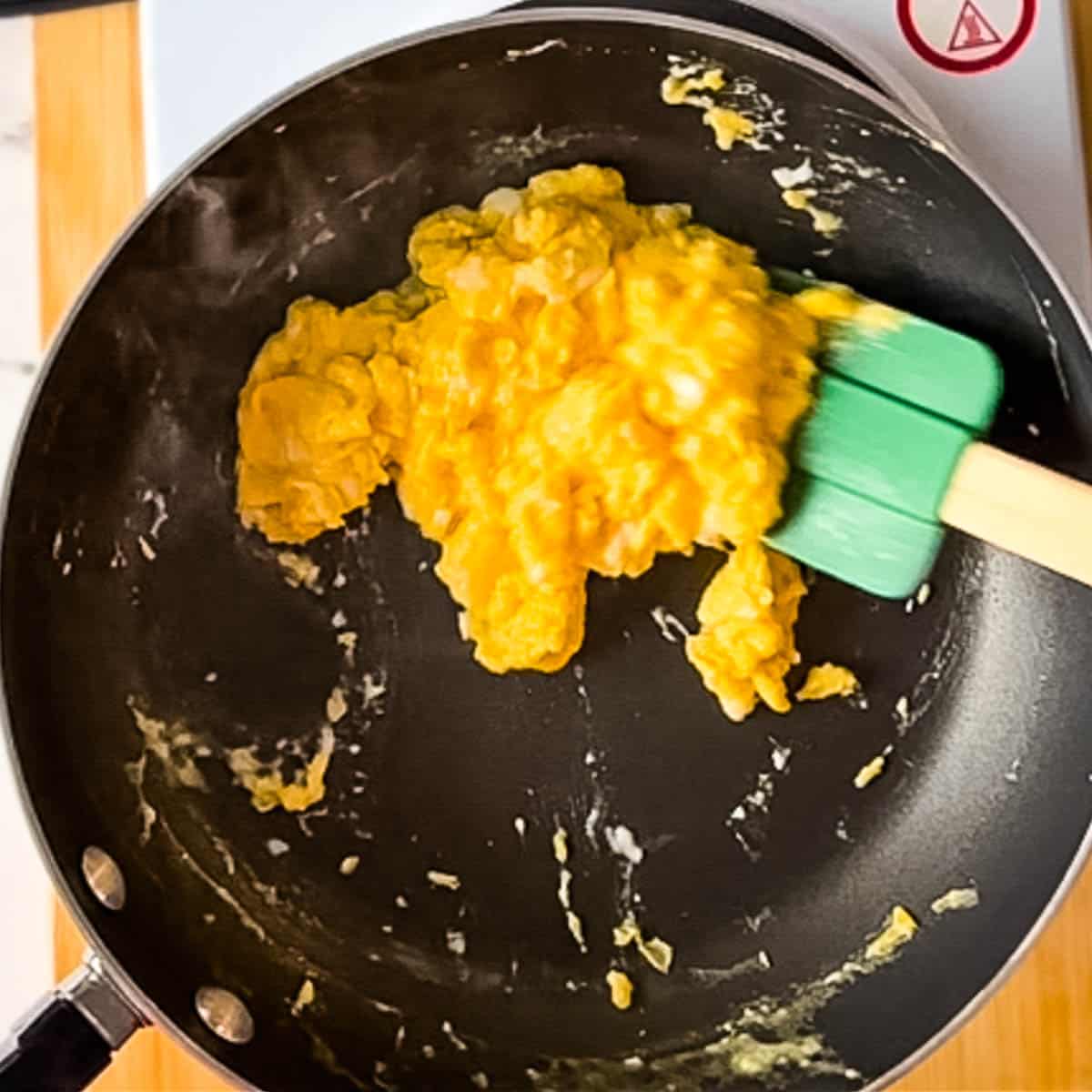 cooked scrambled eggs are scooped out of the pan with a rubber spatula.