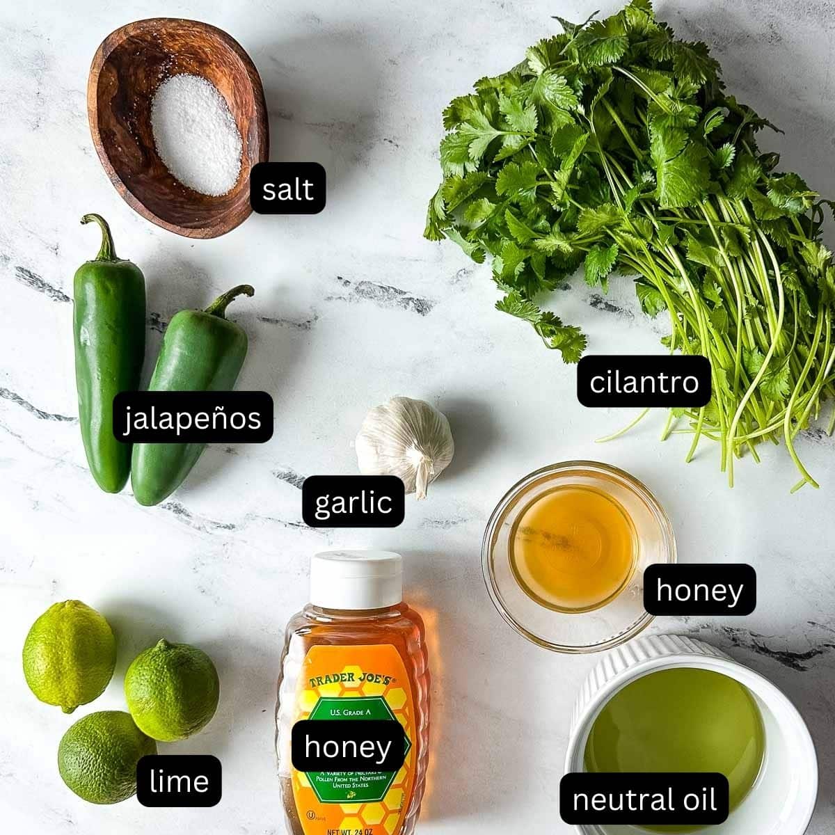 The labeled ingredients for honey jalapeno lime vinaigrette sit on a white marble counter.