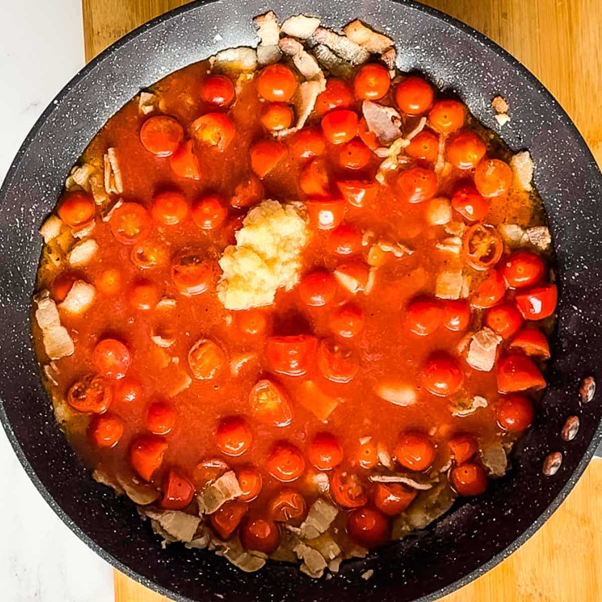 horseradish, tomato juice, and worcestershire sauce are added to cooking cherry tomatoes, bacon, and garlic in pan.