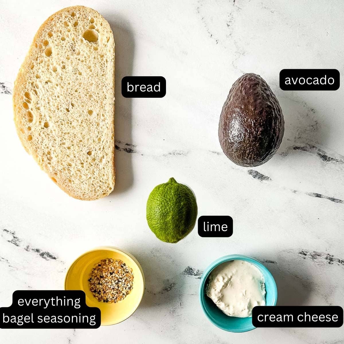 the labeled ingredients for the avocado tartine sit on a white marble counter.