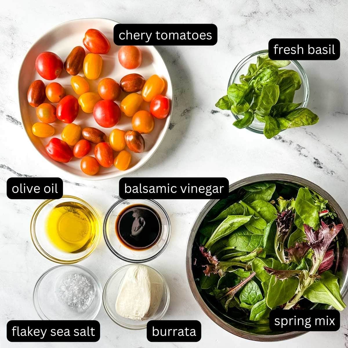labeled ingredients for burrata salad with balsamic glaze on a white marble counter.