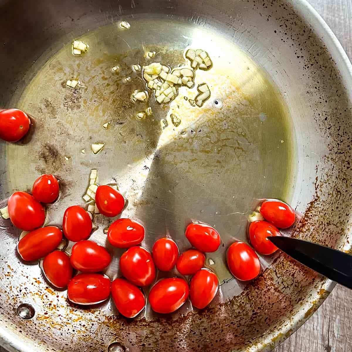 Cherry tomatoes in a stainless steel pan pierced with a paring knife.