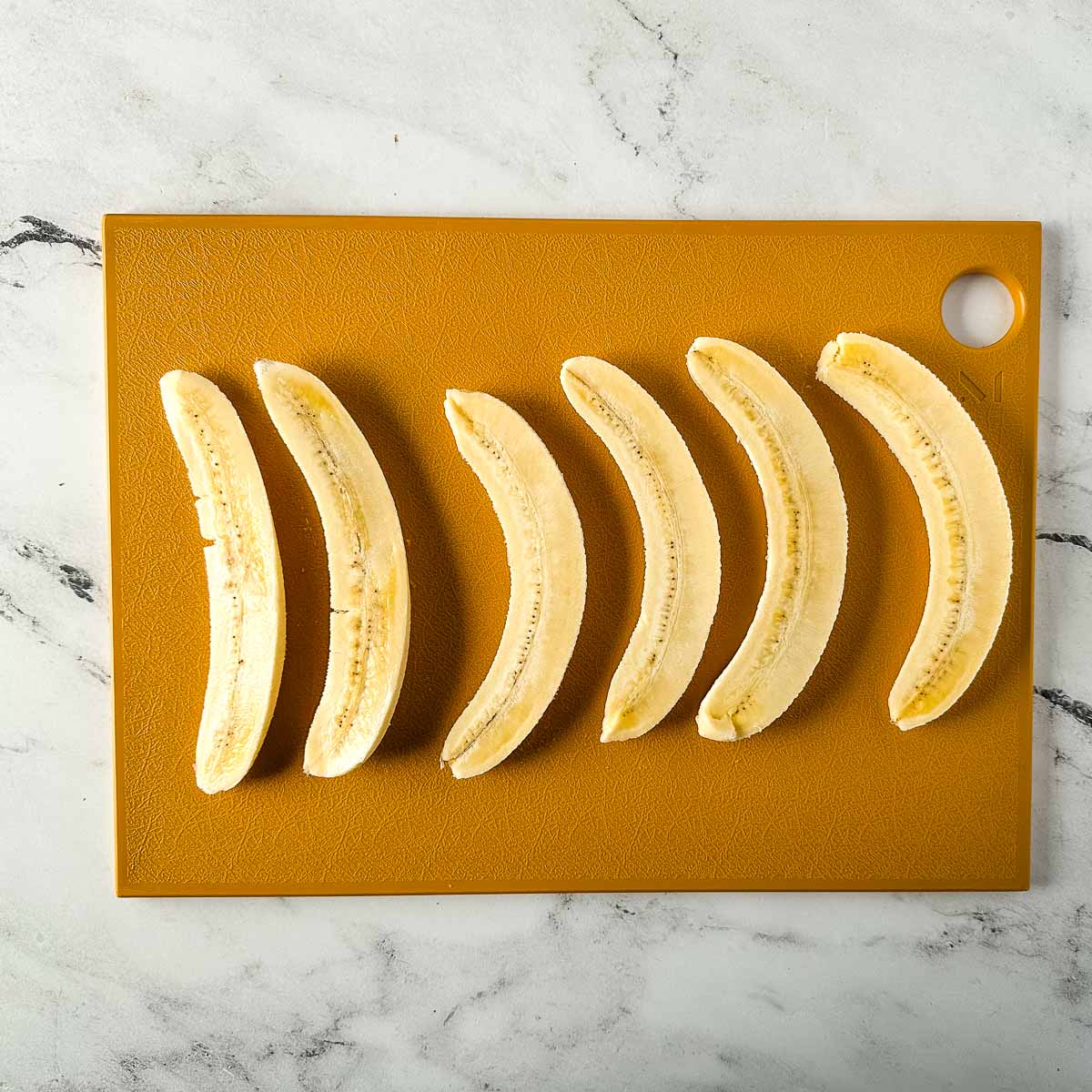 Halved bananas sit on a yellow cutting board.