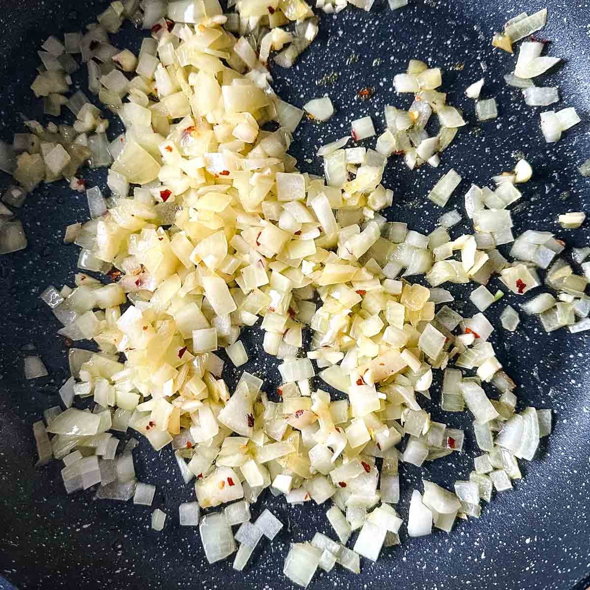 garlic and chili flakes are added to the onion sweating in a frying pan.