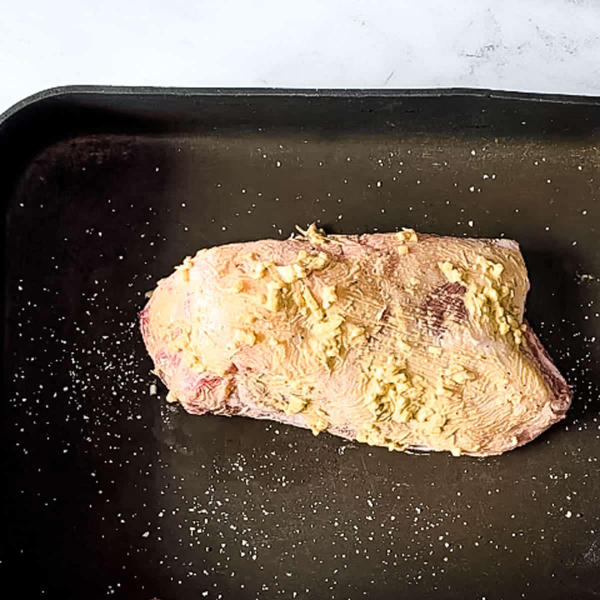 lamb breast rubbed with garlic mustard mixture in roasting pan.
