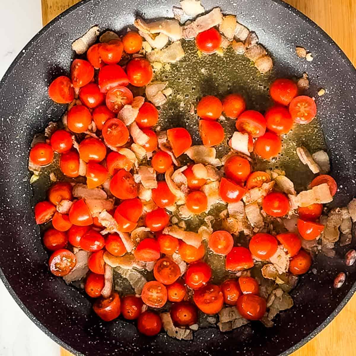 vodka, halved cherry tomatoes, bacon, and garlic cooking in pan.