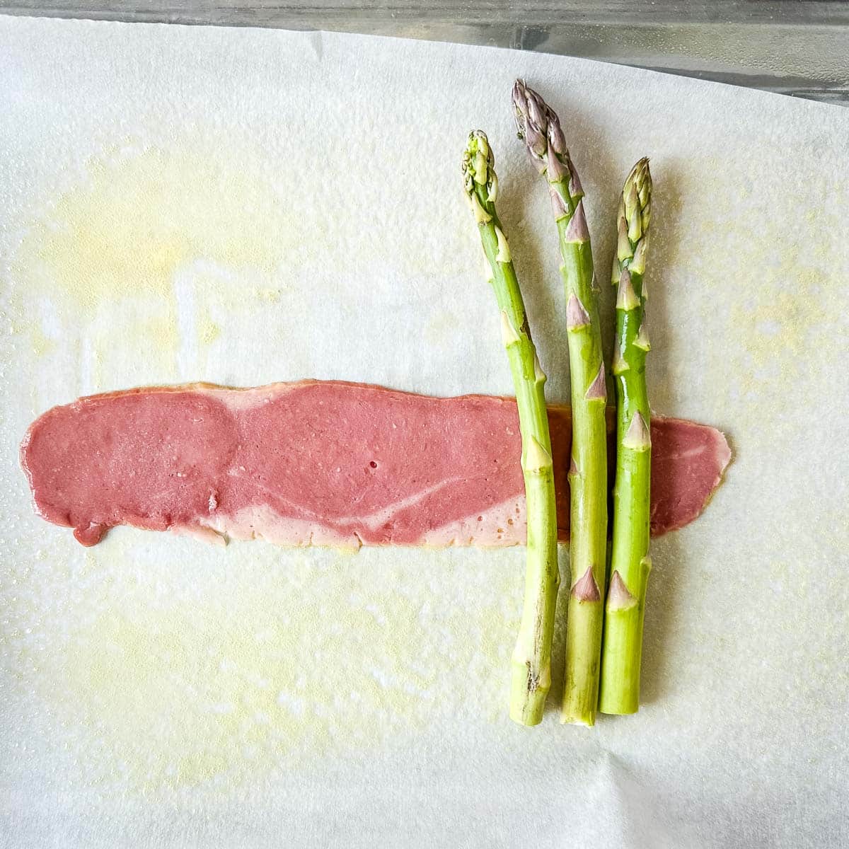 three asparagus spears sit crosswise on a trip of turkey bacon.