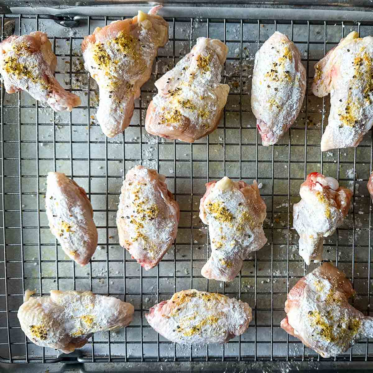 Chicken wings tossed in lemon pepper, lemon zest, and baking powder on a wire rack.