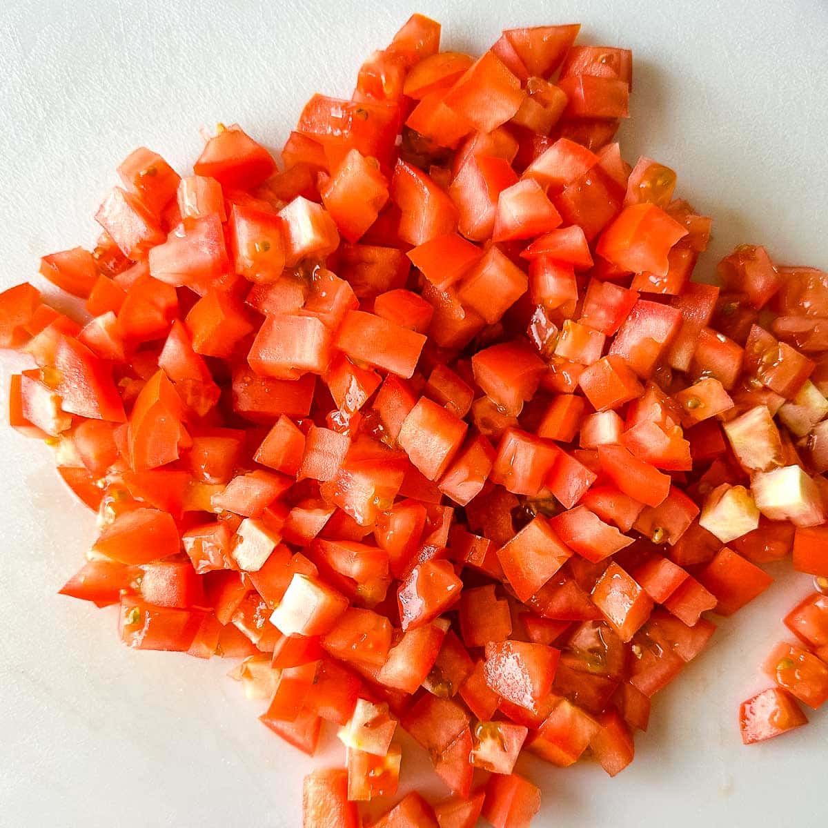 Chopped roma tomatoes on a white cutting board.