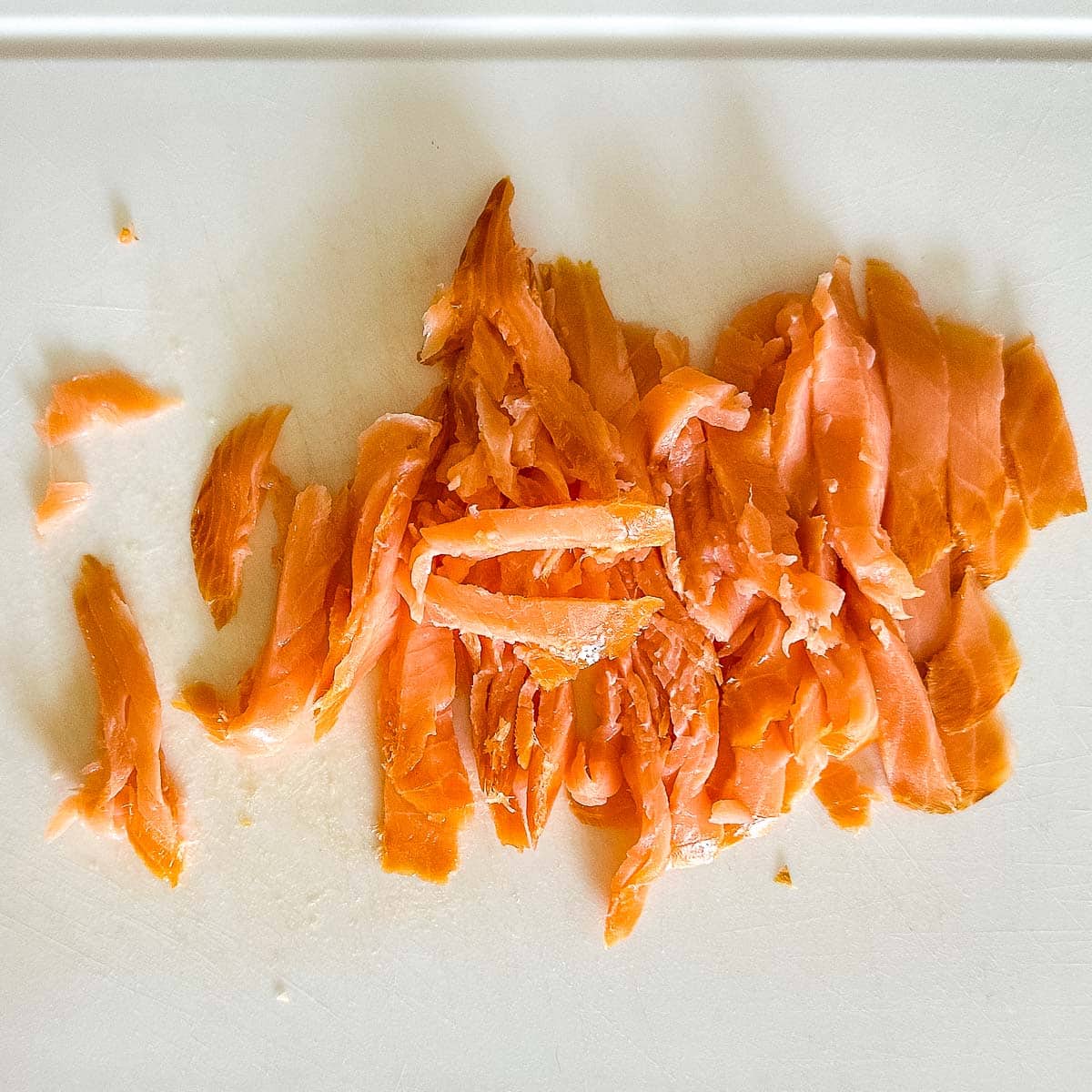 chopped smoked salmon on a white cutting board.