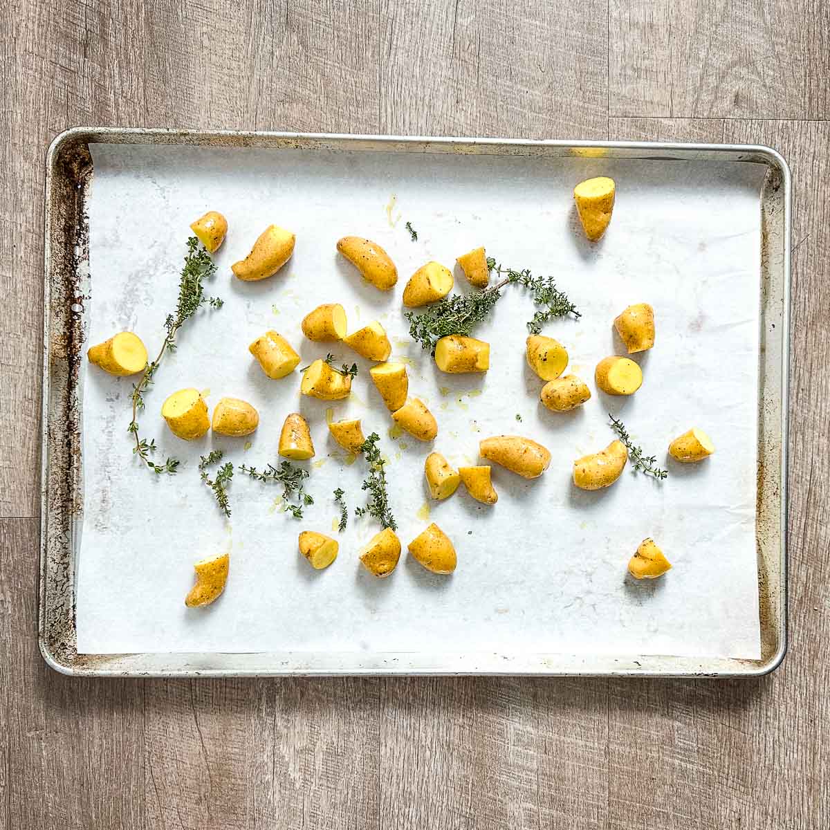 Halved fingerling potatoes and thyme sprigs on a sheet tray.