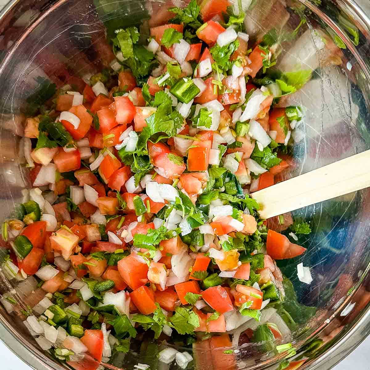 Garden fresh salsa is mixed in a stainless steel bowl.