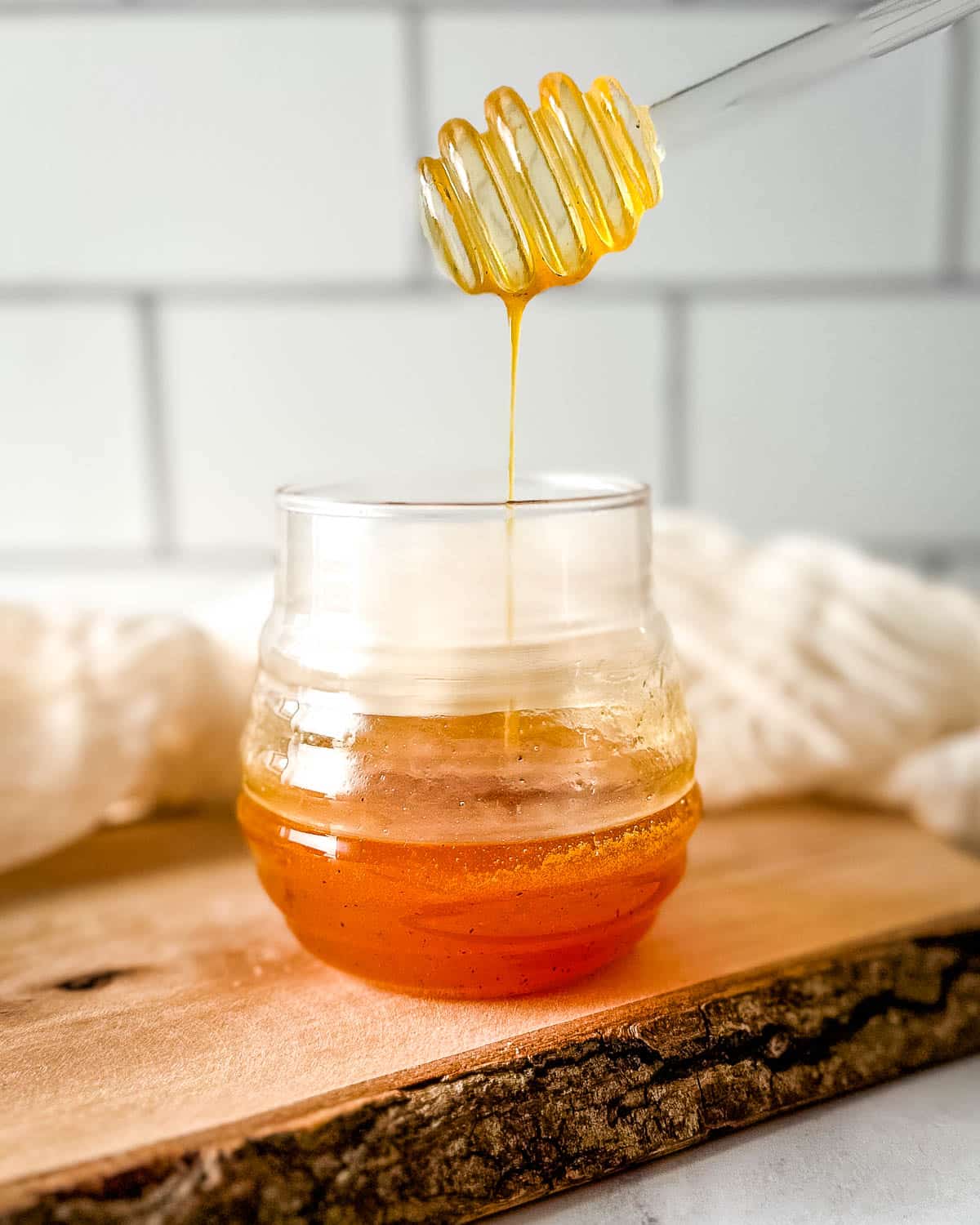 Hot honey sauce is drizzled into a glass jar with a glass honey dipper.