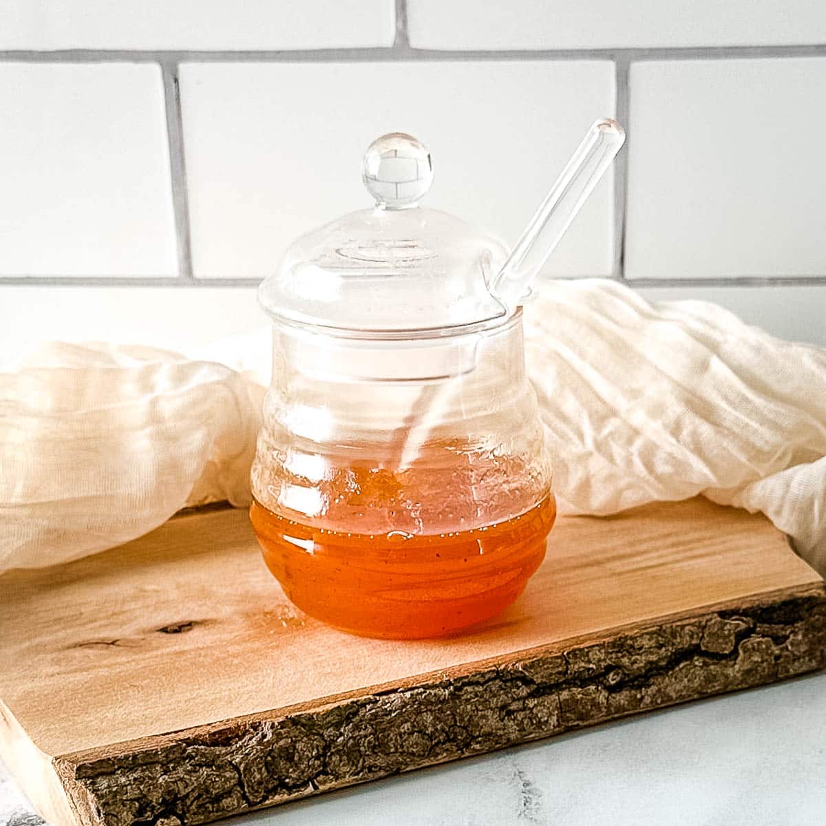 Hot honey sauce in a glass jar on a rustic wooden cutting board with a white linen.