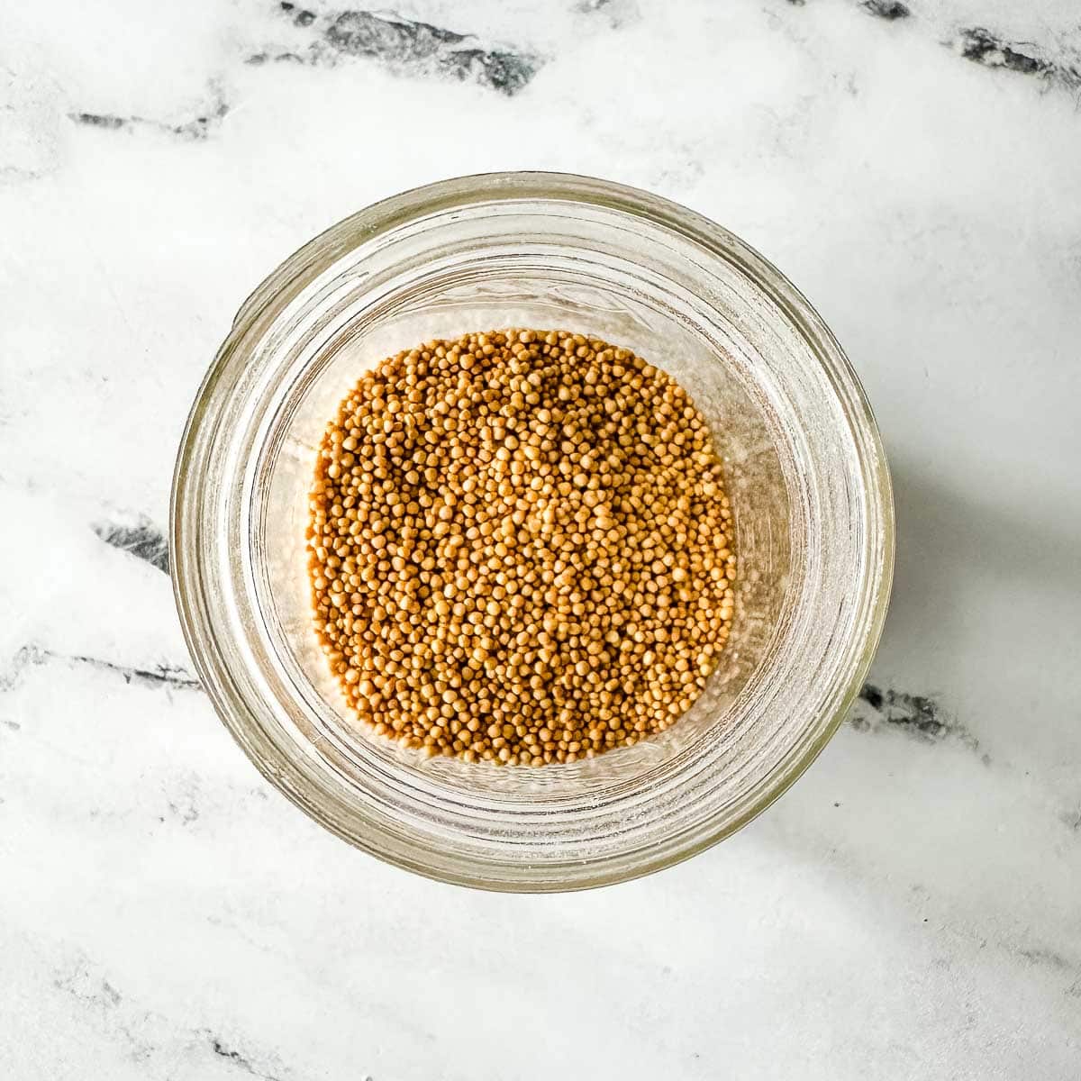 Overhead view of yellow mustard seeds in a glass jar.
