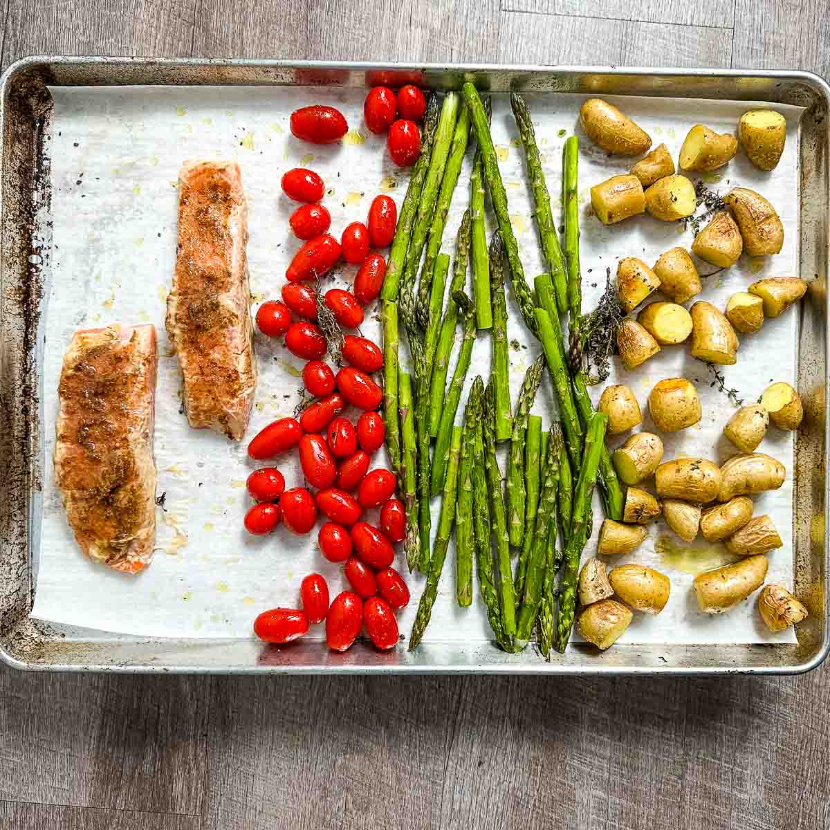 Salmon, cherry tomatoes, asparagus, and fingerling potatoes on lined sheet pan.