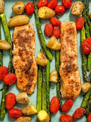 Closeup overhead shot of roasted salmon, asparagus, fingerling potatoes, and cherry tomatoes on a blue sheet tray.