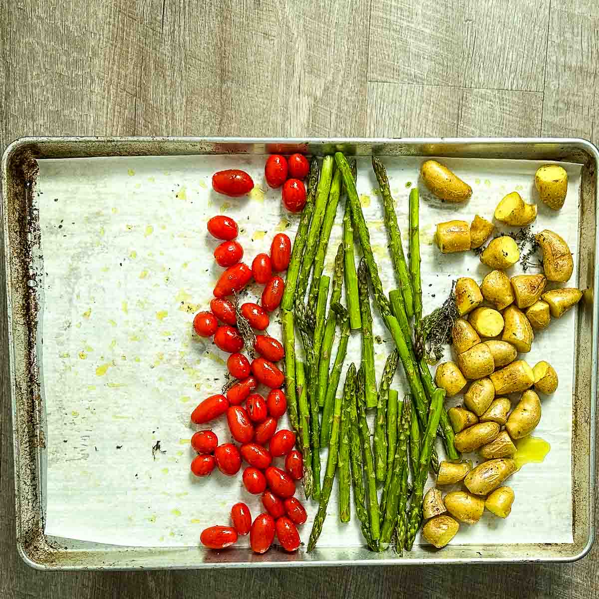 A lined sheet pan with half-roasted fingerling potatoes, asparagus, and cherry tomatoes.
