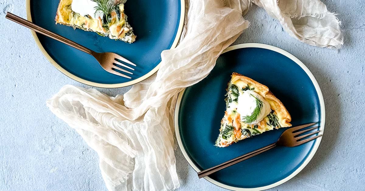 two slices of smoked salmon and spinach quiche on dark blue plates.