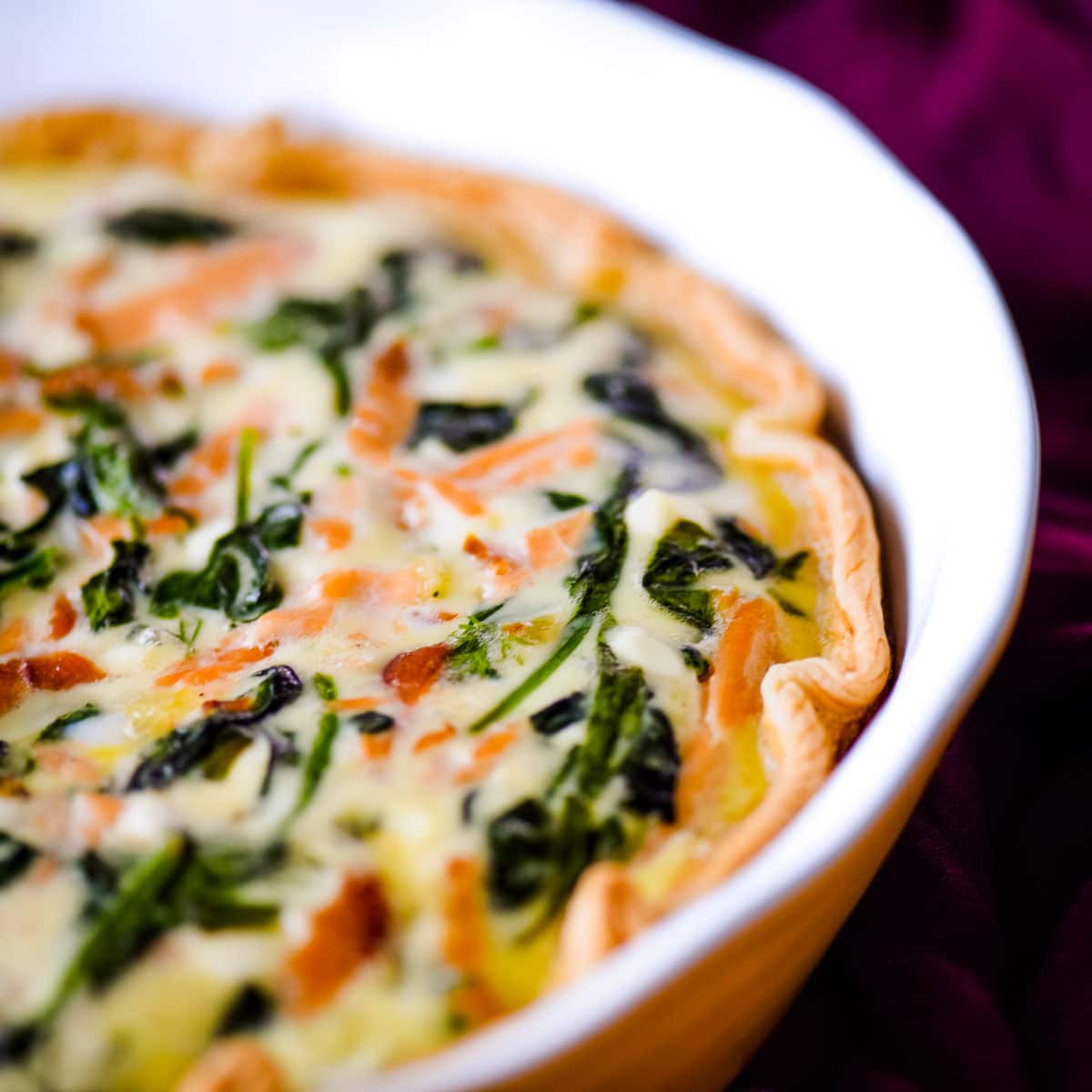 closeup side view of salmon spinach quiche in a yellow pie dish.