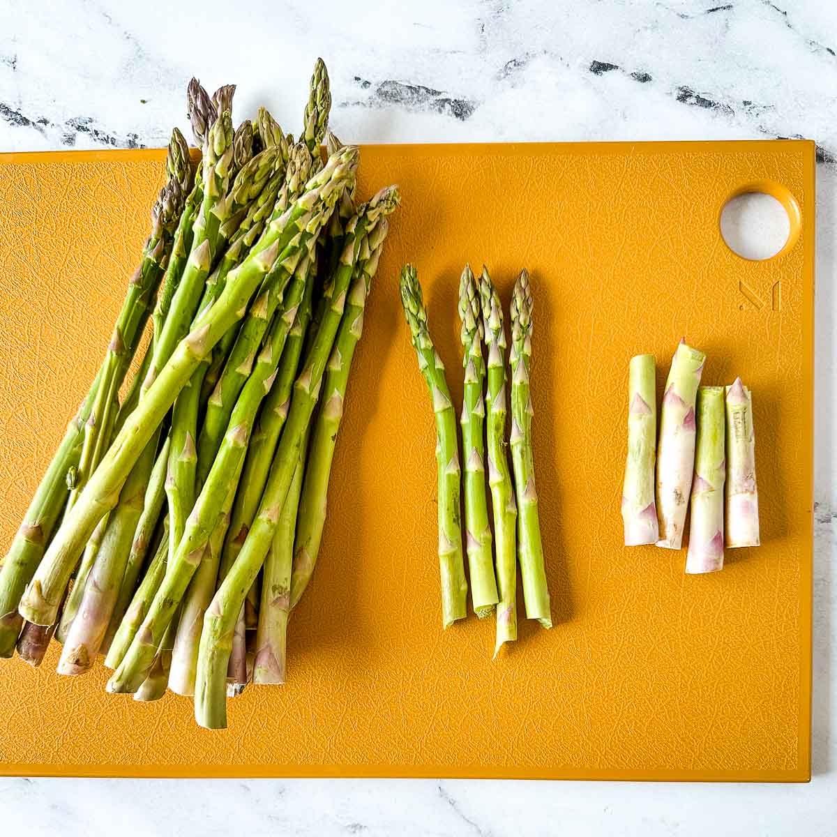 asparagus is trimmed on a yellow cutting board.