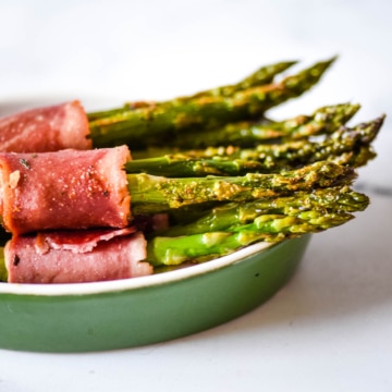 side view of turkey bacon wrapped asparagus in a green dish.