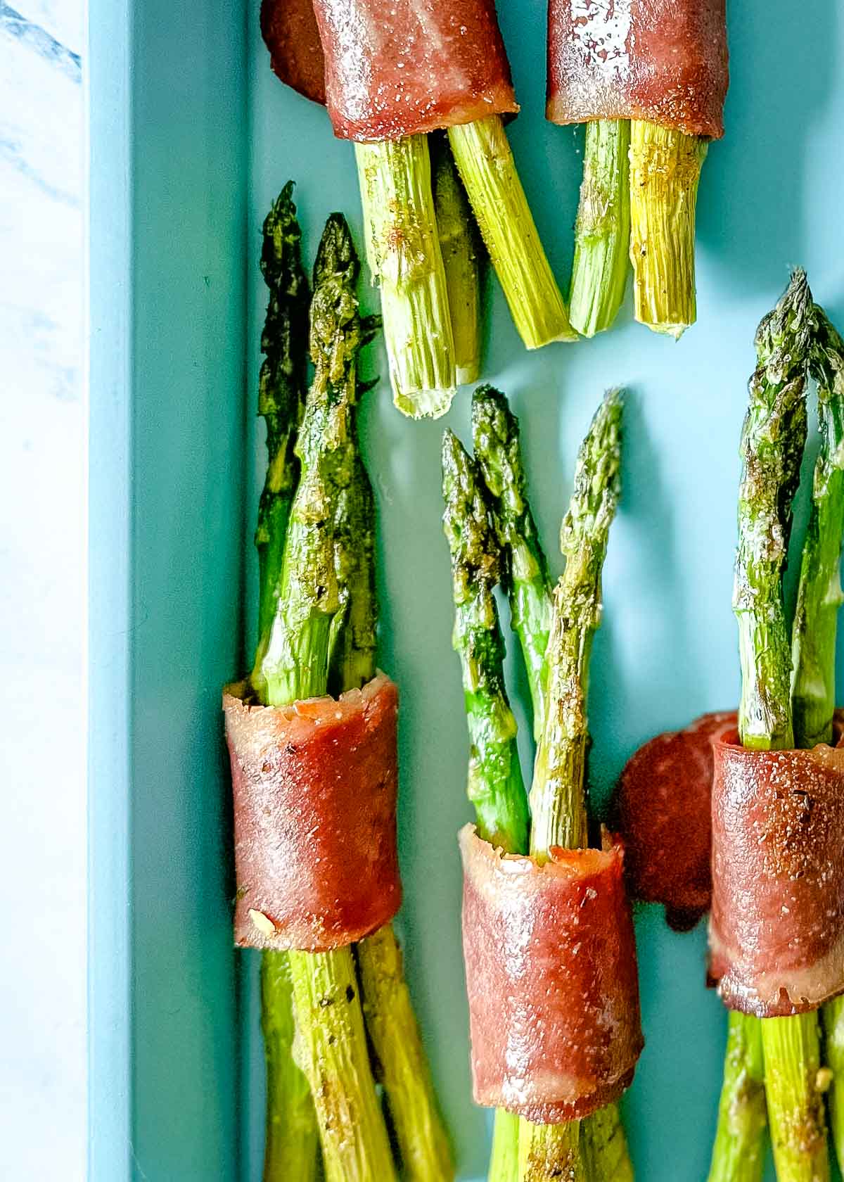 turkey bacon wrapped asparagus bundles on a blue sheet tray.