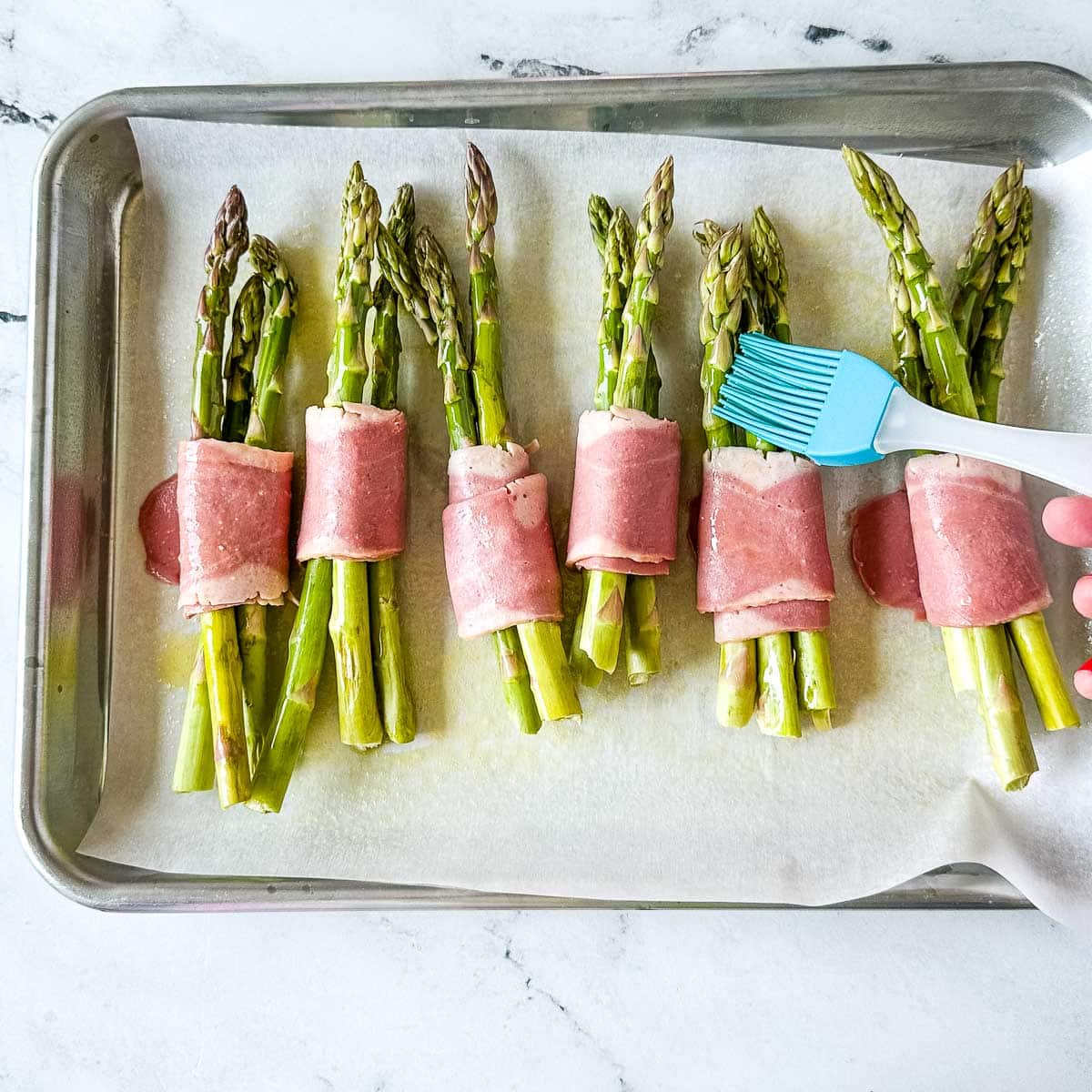 brushing turkey bacon wrapped asparagus bundles with olive oil.