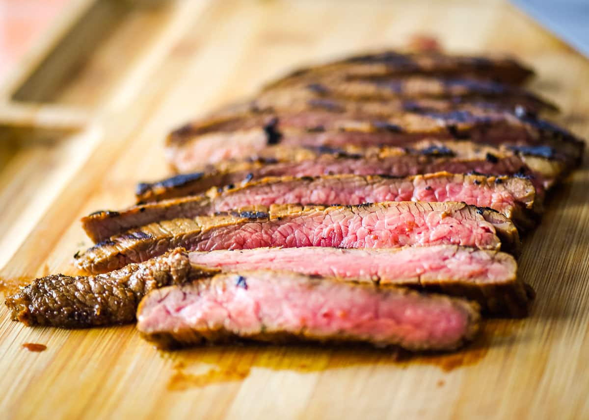 A closeup shot is shown of sliced carne asada on a wooden cutting board.