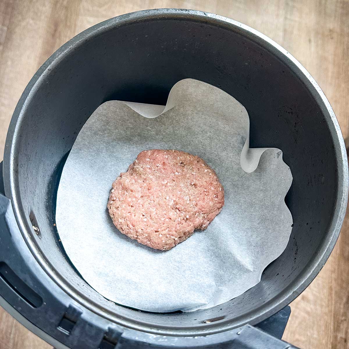 A raw air fryer turkey burger is shown in the air fryer basket lined with parchment paper.