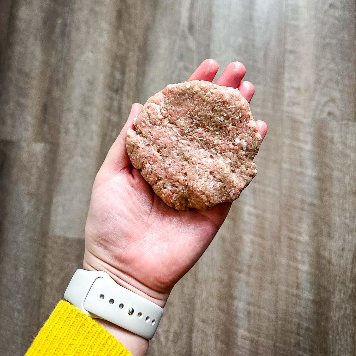 A formed turkey burger is held over a wooden backdrop.