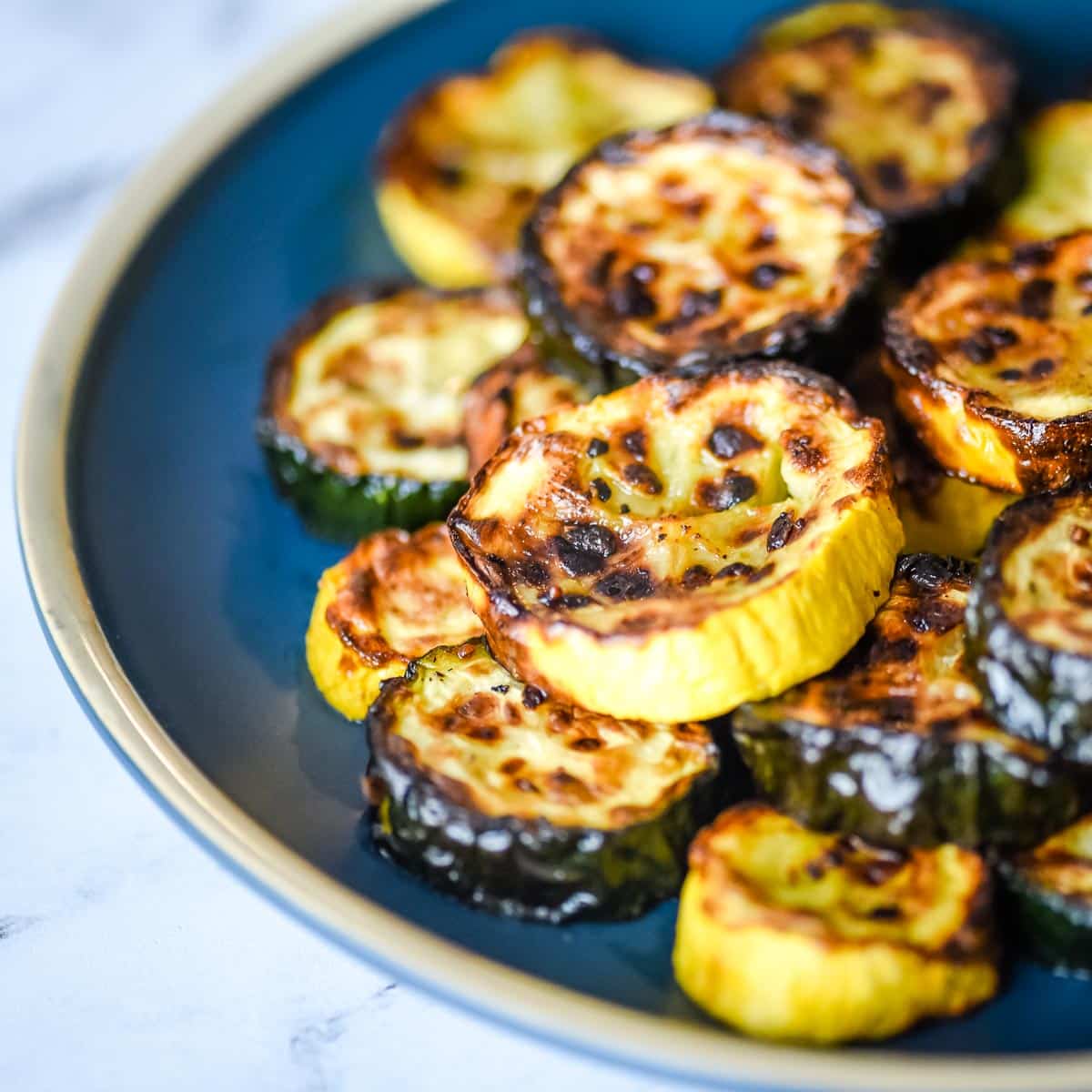 Closeup side view of air fryer zucchini and squash on a blue plate.