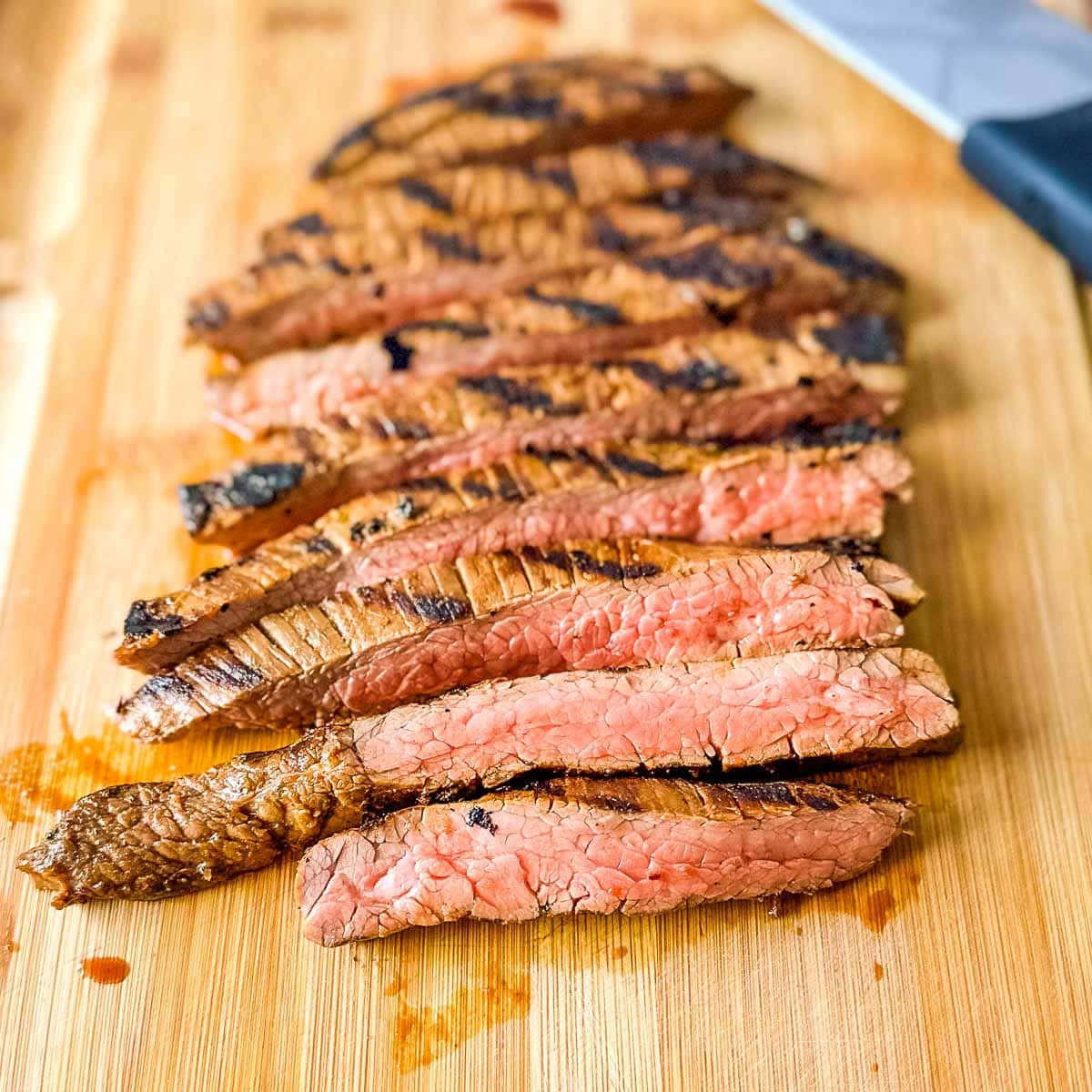 A closeup shot shows sliced carne asada on a wooden cutting board.
