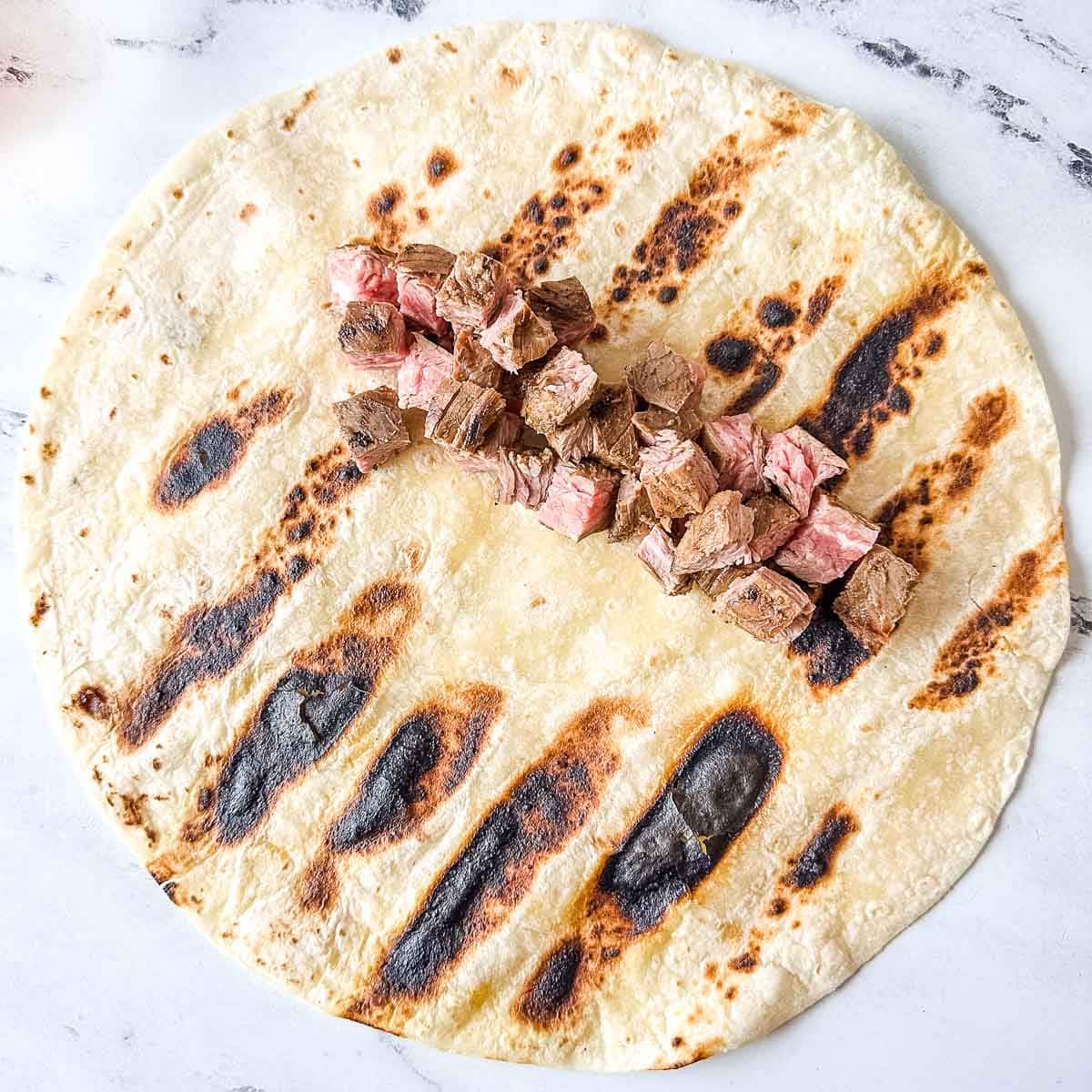 Diced carne asada pieces sit on top of a grilled tortilla.