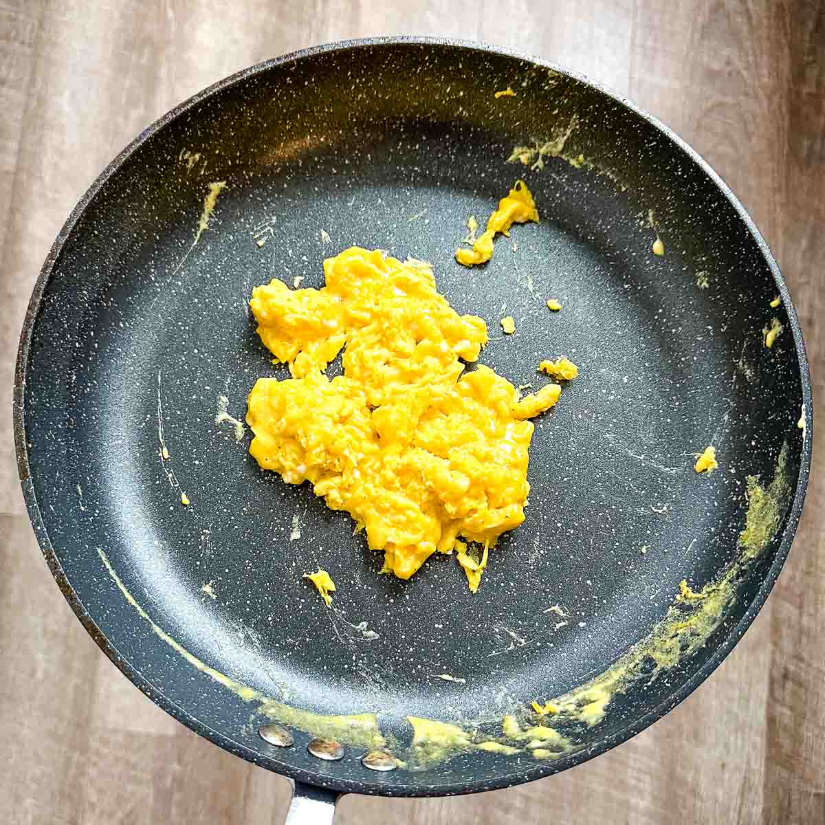 Cooked cheesy scrambled eggs sit in a black frying pan.