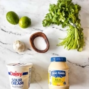 The ingredients for cilantro lime crema on a white marble counter.
