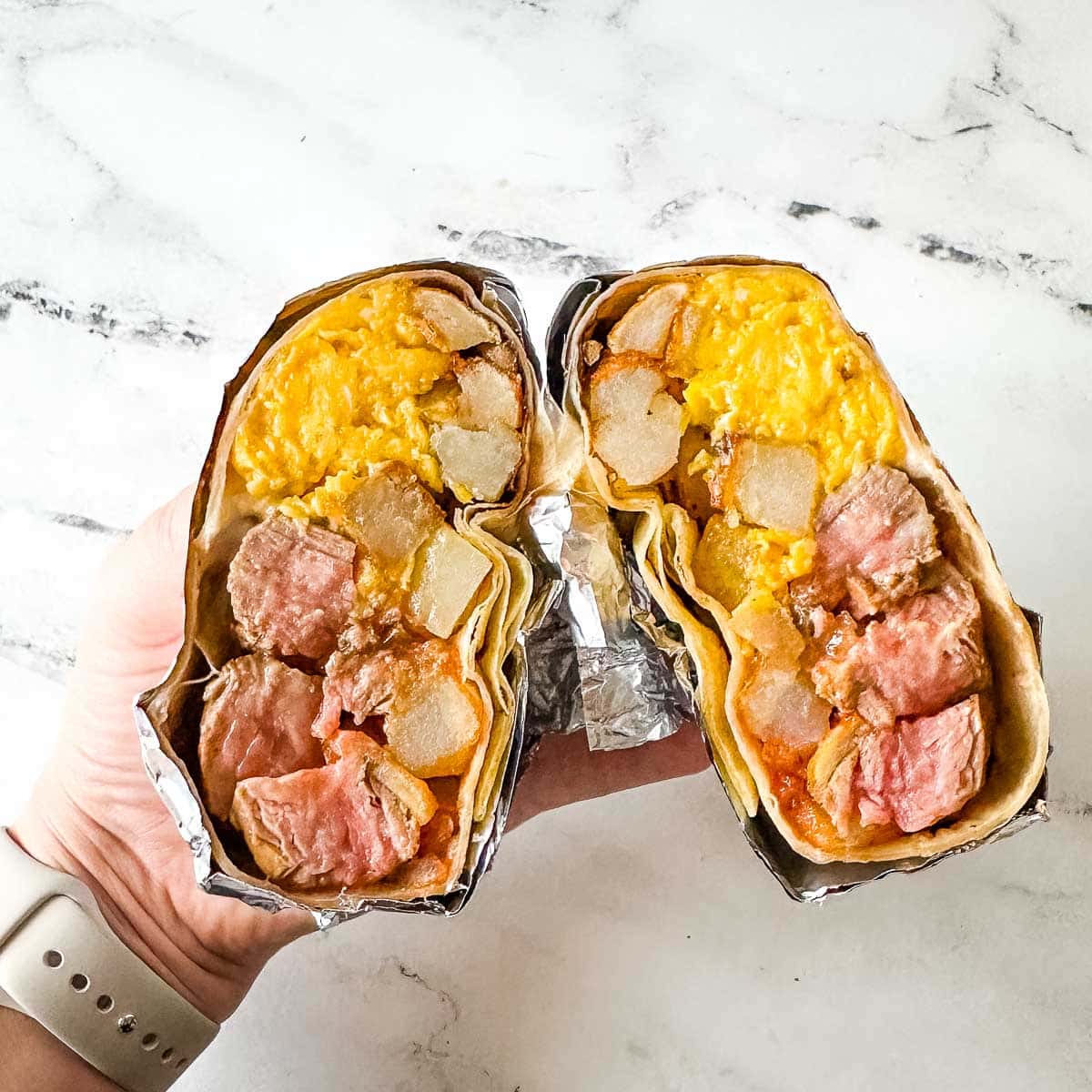 Carne asada burrito that is wrapped in foil and cut in half to expose the center of the burrito.
