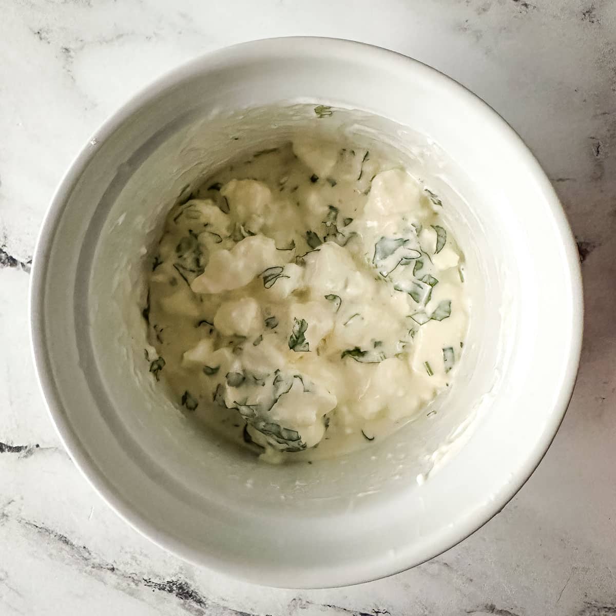 Cotija cheese, mayonnaise, sour cream, cilantro, and lime juice mixed in a white bowl.