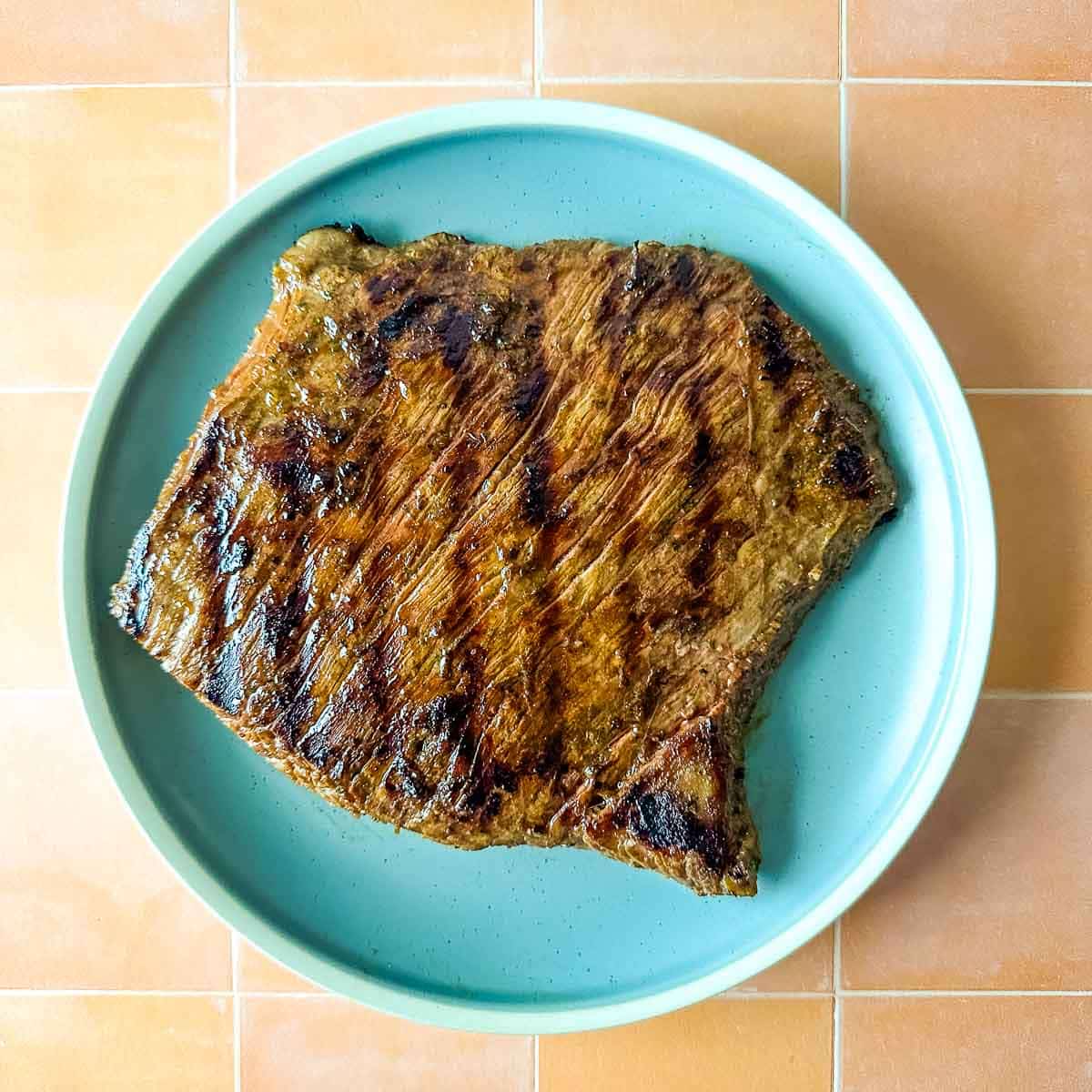A grilled steak sits on a light blue plate.
