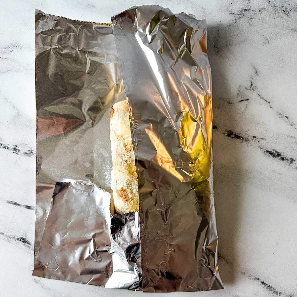 The bottom portion of the foil and the right vertical edge of foil are folded over the carne asada burrito.
