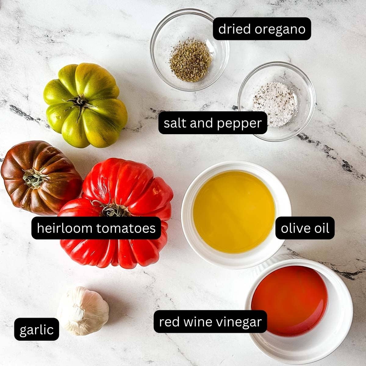 labeled ingredients for marinated heirloom tomatoes on a white marble counter.