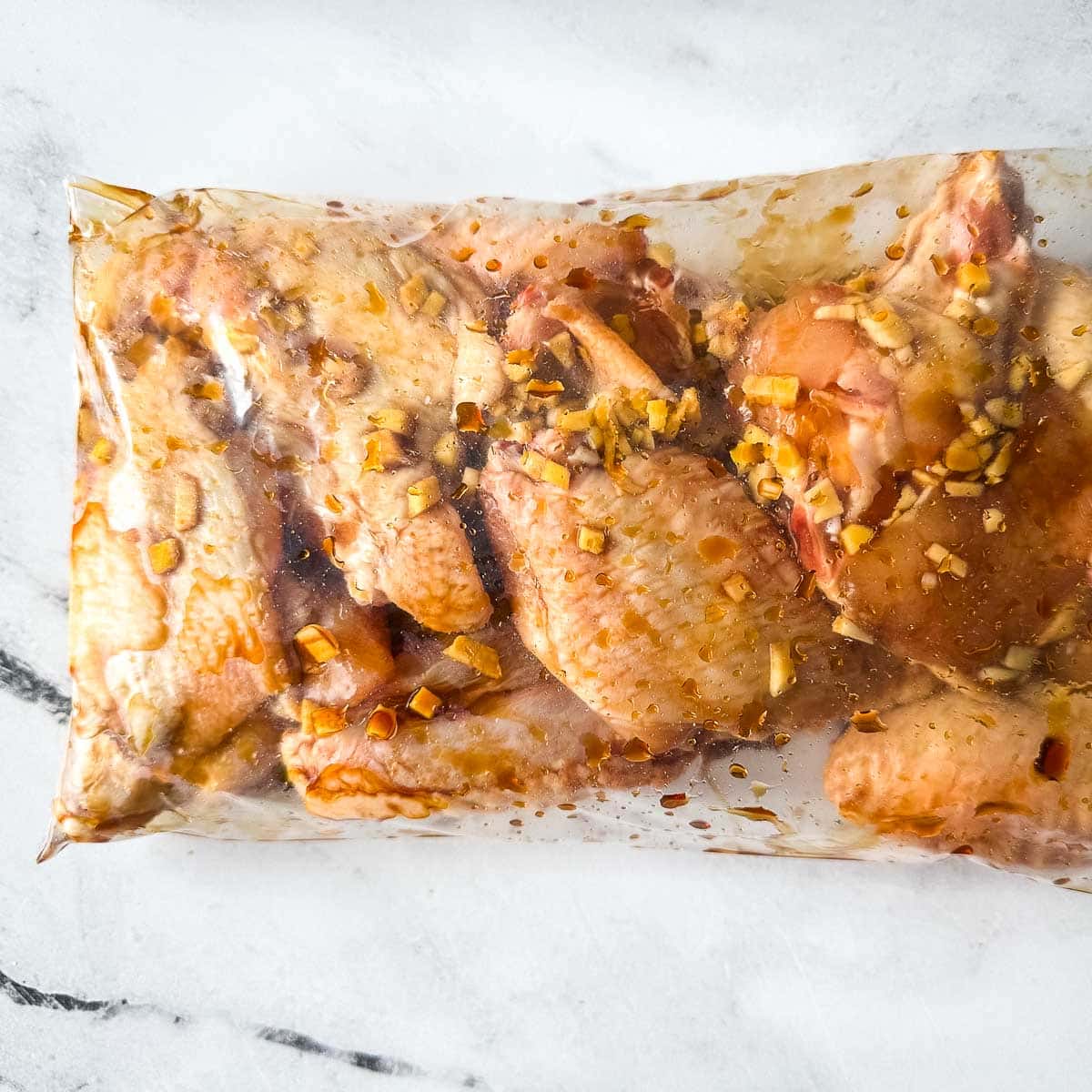 Chicken wings are marinated in a plastic bag with soy garlic ginger marinade.