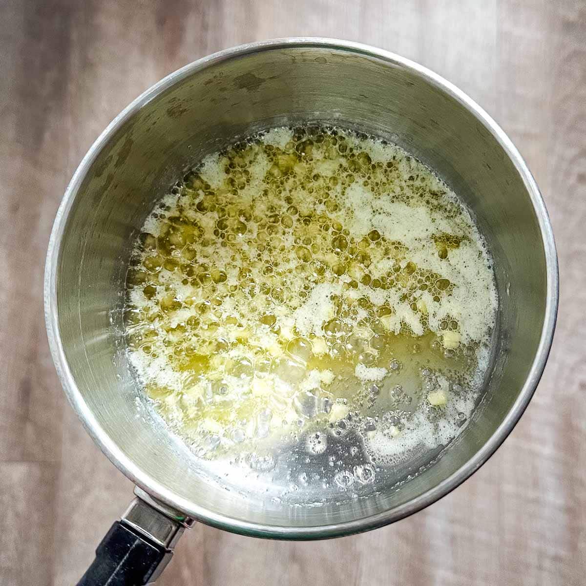 Garlic cooks in a saucepan with melted butter.