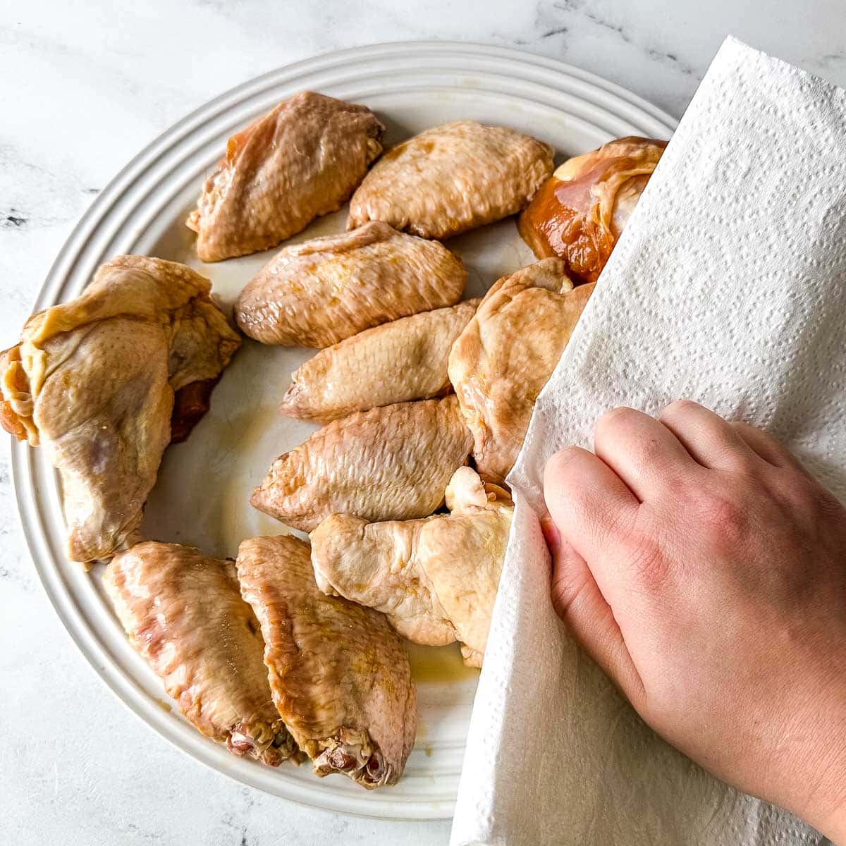 Patting raw soy garlic chicken wings dry with a paper towel.