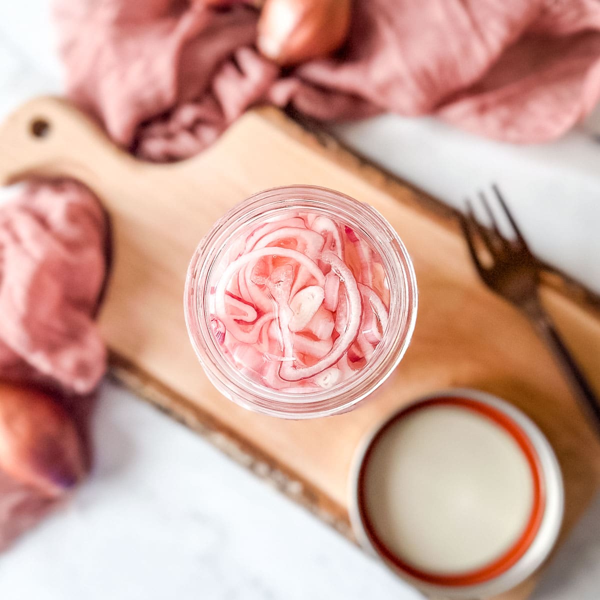 Quick pickled shallots in a glass jar on a rustic wooden cutting board.