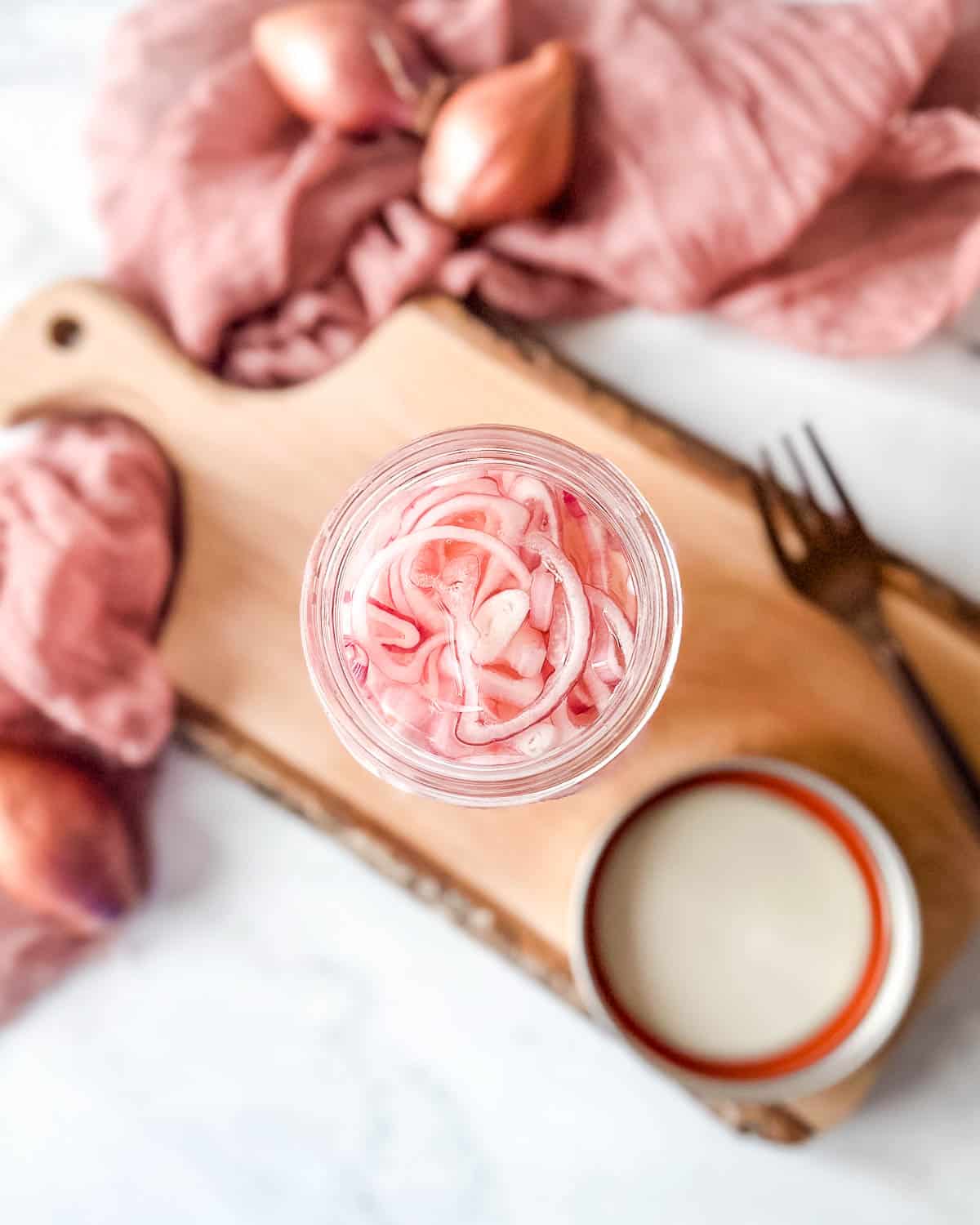 Quick pickled shallots in a glass jar on a rustic wooden cutting board.