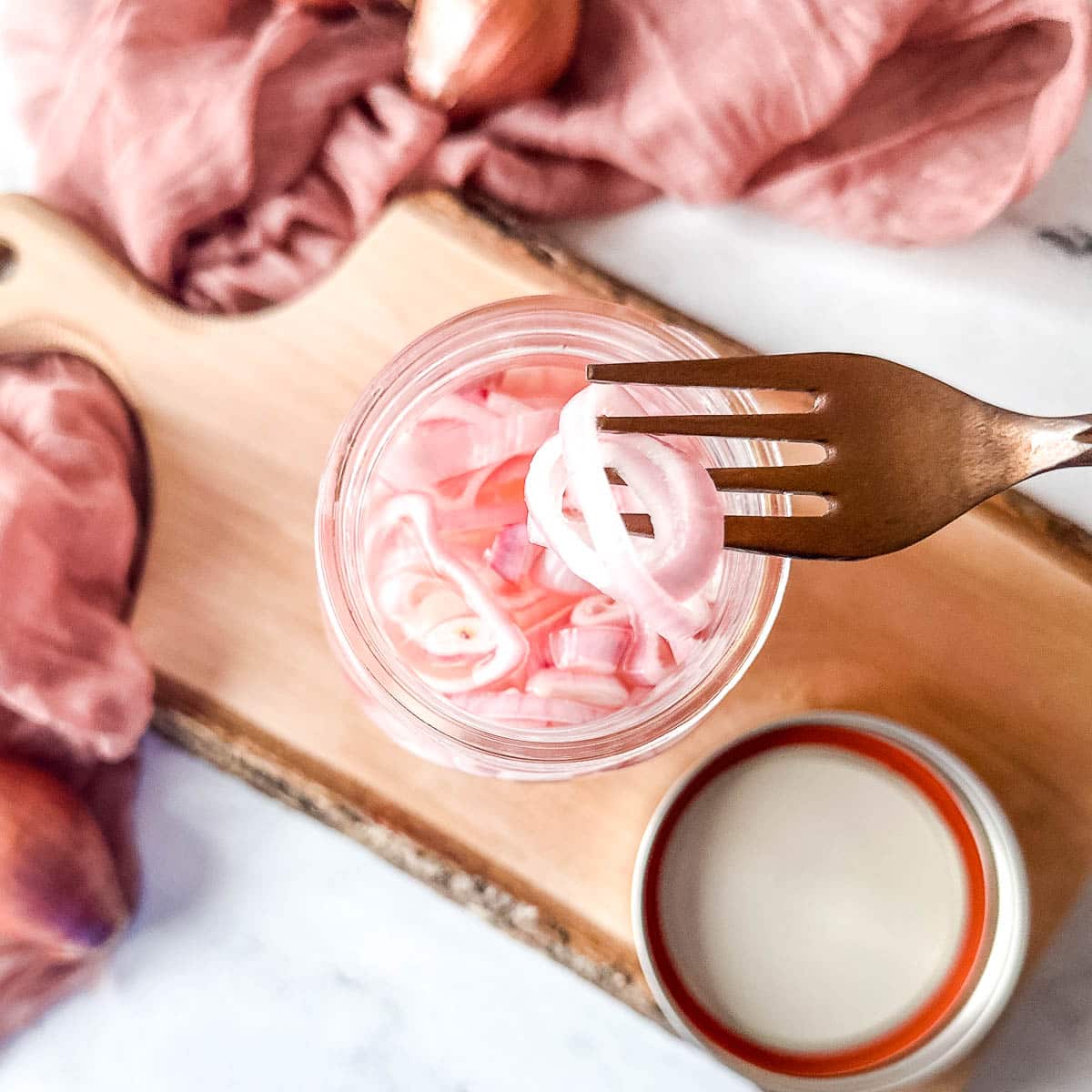 A few slices on quick pickled shallots are held over a jar with a copper-colored fork.