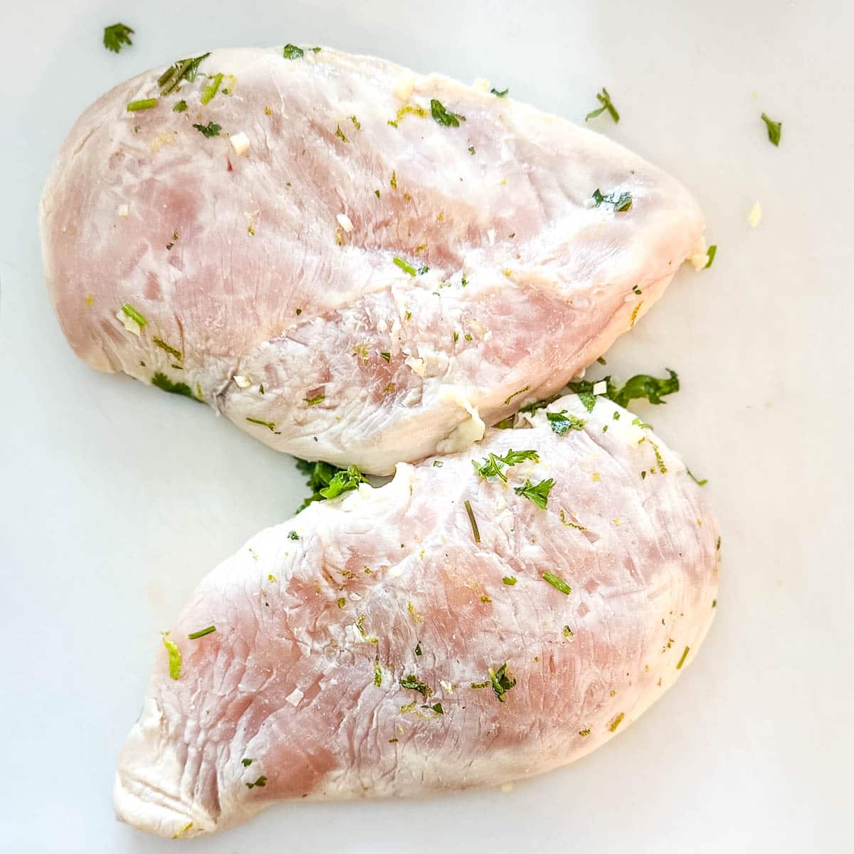 Raw marinated chicken on a white cutting board.